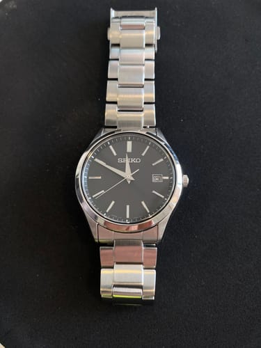 Reseñador mostrando el elegante reloj Seiko SBPX147 sobre una superficie oscura.
