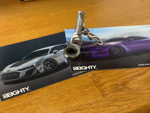 Customer's shiny 80Eighty 10mm Wrench Keychain resting on branded cards on a wooden table.