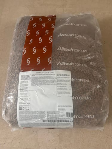 Recensent toont de grote, doorzichtige zak met Alltech Coppens Premium Carp Pellets.
