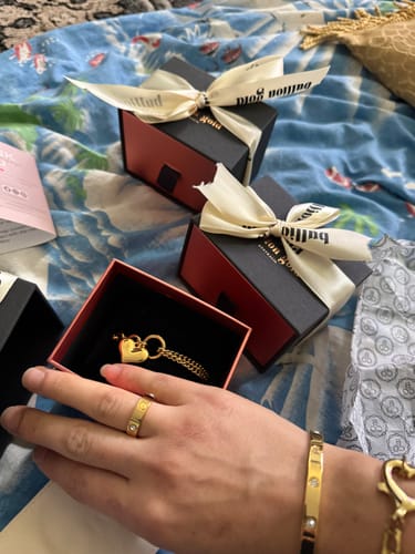 Customer's hand wearing the Bullion Gold Carrie Ring, with matching jewelry and packaging in the background.