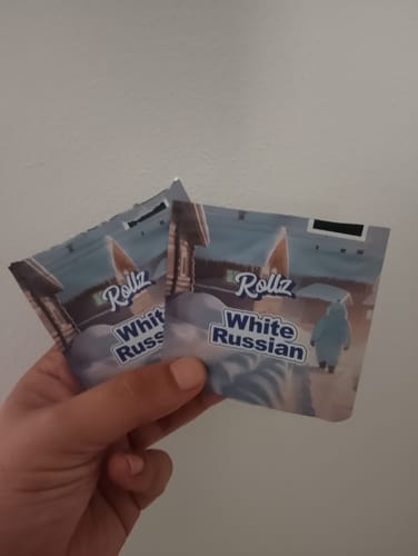Customer's hand holding two packets of White Russian THCA Flower against a plain background.