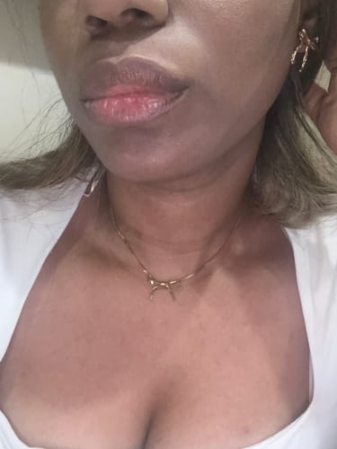 Close-up of a reviewer wearing the gold Carol Bow Necklace and a matching bow earring from the bundle.