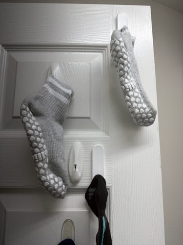 Reviewer's grey Dual-Direction Grip Stripes socks hanging on a door, showing the non-slip grips.
