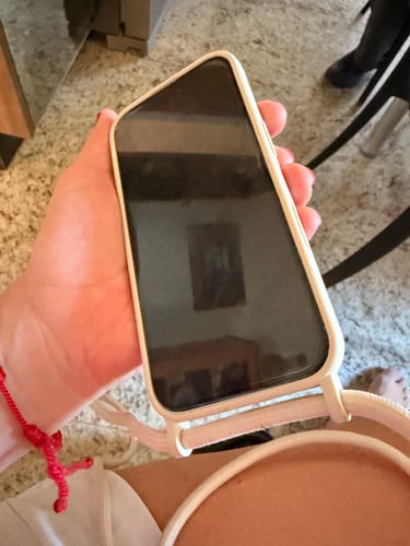 Cliente segurando um celular com a Cordinha Odara creme e a capinha combinando.