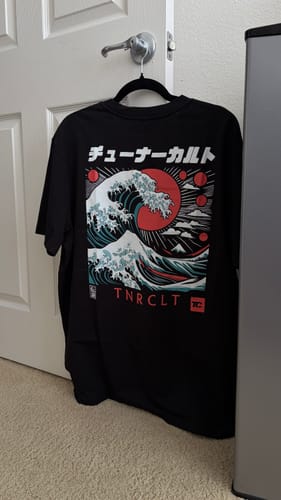 Reviewer's black RISING TIDES TEE on a hanger, showing the back with a detailed Japanese wave graphic.
