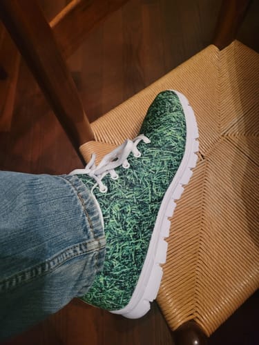 Customer wearing the Golf Course Grass Print Running Shoe, resting their foot on a woven chair.