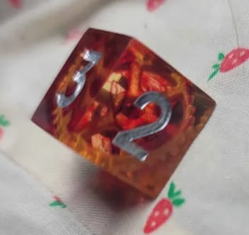 Customer's close-up of a reddish-orange URWizards D&D gear resin die, showing the internal gears and silver numbers.