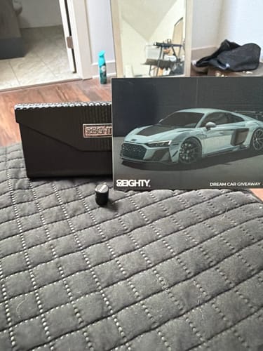 Reviewer's single black 80Eighty Valve Stem Cap on a dark quilted surface, next to a promotional card.