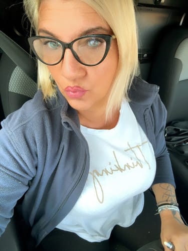 Reviewer in a car wearing black glasses, showing the bright blue color of her Topaz contact lenses.