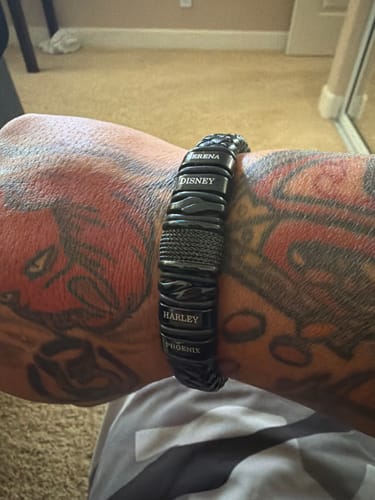 Reviewer wearing the personalized black bracelet on a tattooed arm, showing engraved names.
