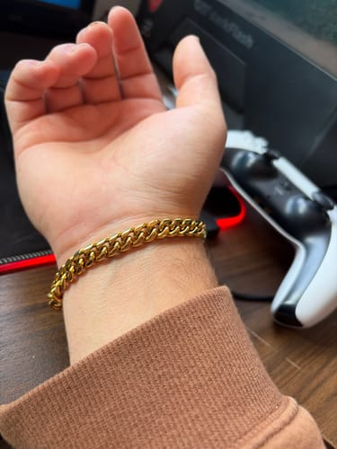Cliente mostrando la Pulsera Cuban Oro de 8mm en su muñeca, con un suéter marrón.