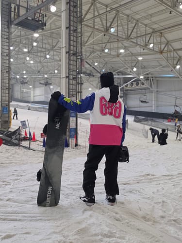 Customer wearing black insulated baggy snow pants at an indoor snow park, holding a snowboard.