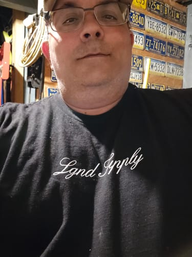 A reviewer wearing a black t-shirt with white script logo from their LGND92 Mystery CASH Box.