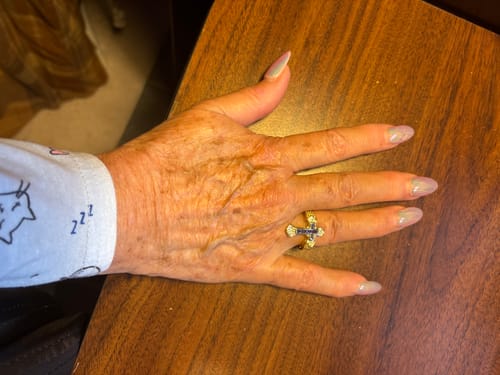 Customer's hand resting on a wooden table, wearing the Central Cross Motif Ring.