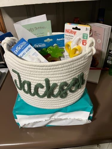 Customer's personalized woven basket with the name 'Jackson' in green, filled with baby shower gifts.