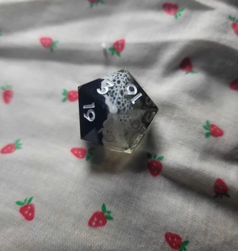 Customer's D20 mystery die, half black and half clear with a white lace-like pattern inside.