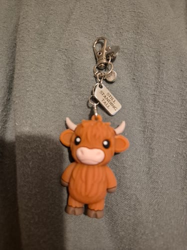 Customer's Highland Cow keychain with a brown resin charm and a small metal tag that says 'Still Standing Tall'.
