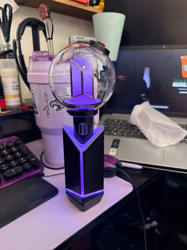 Reviewer's BTS Official Light Stick Ver.4 and cradle glowing with purple light on a desk.