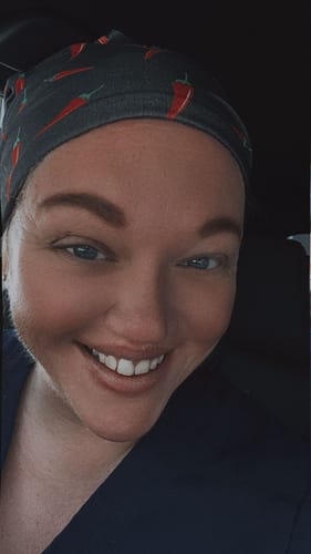 Close-up of a reviewer smiling while wearing the DuoStyle Scrub Hat with a chili pepper pattern.