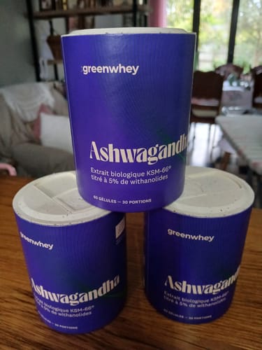Un client montre trois pots violets d'Ashwagandha bio KSM-66 empilés sur une table en bois.