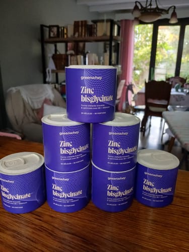 Photo d'un client montrant son stock de sept boîtes de Zinc Bisglycinate empilées sur une table en bois.