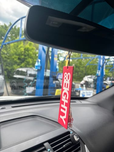 A customer's red 80Eighty air freshener hanging from a car's rearview mirror.