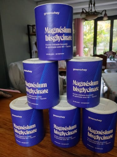 Un client montre six pots de Magnésium Bisglycinate empilés en pyramide sur une table.