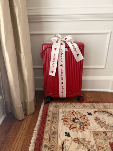 Customer's red All-in-One Carry-On shown as a gift, wrapped with a large white ribbon.
