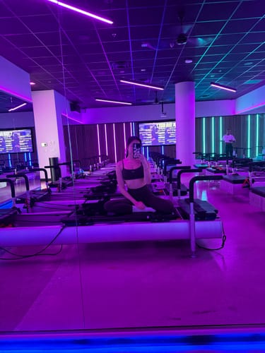 Reviewer taking a mirror selfie in a purple-lit fitness studio, wearing the Espresso Micro Bra and matching leggings.