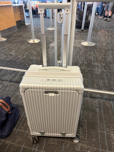 Customer's silver, ribbed Carry-On: All-in-One Expandable suitcase with its handle extended in an airport terminal.