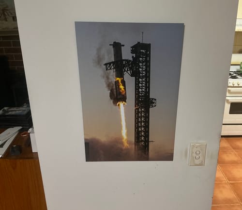 Customer's 'IFT5 - Coming in Hot' print of a rocket launch hanging on a white wall in a room.