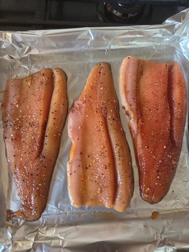 Customer's three raw trout fillets on a baking sheet, seasoned with SPG rub from the Rub Combo Shakers pack.