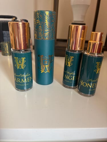 Reviewer's travel-size Carmen perfume shown alongside other scents from the brand on a white tabletop.