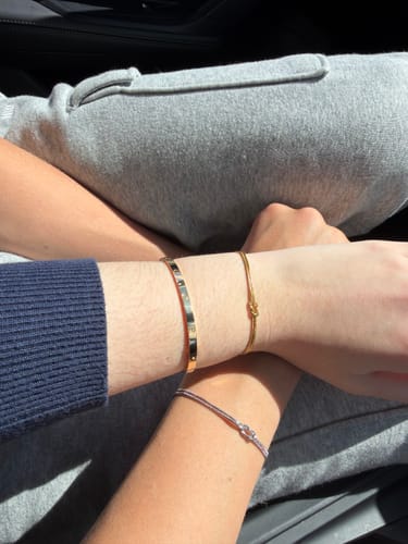 Reviewer's photo showing a gold and a silver Forever Knot Bracelet on two different wrists, crossed with a third.