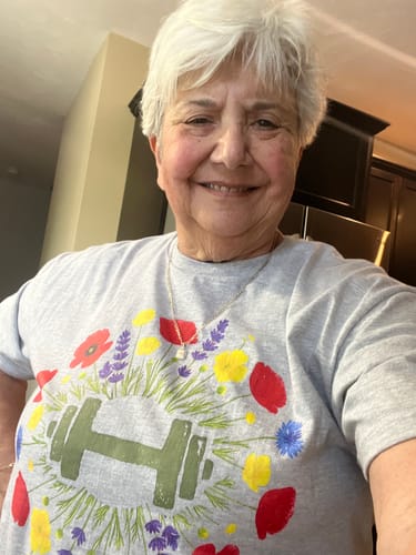 Reviewer smiling while wearing the grey Wildflower Dumbbell T-Shirt, showing the colorful floral graphic.