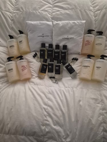 Reviewer's large collection of Thomson Carter fragrances and body products displayed on a white comforter.