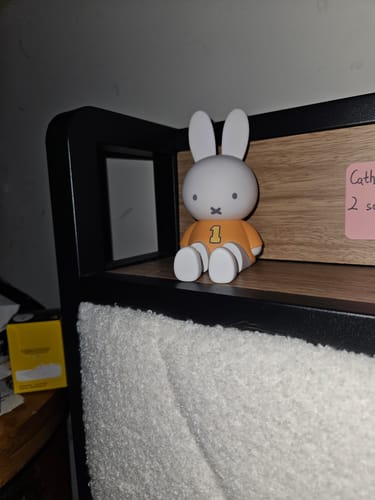 Customer's Miffy Figure Phone Stand with an orange shirt sitting on a bedside shelf.