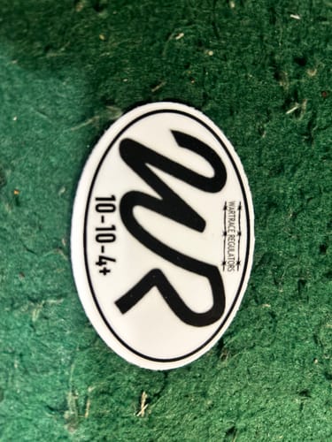 Customer's oval custom sticker with a black 'WR' logo design, placed on a textured green surface.