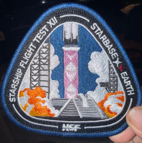 Reviewer holding the embroidered Starship Flight 12 Collectors Patch, which depicts a rocket launching between two towers.