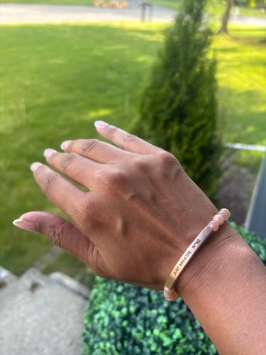 Reviewer's hand wearing a Sunstone Custom Bracelet with a gold bar engraved 'JUST BREATHE - N°50' outdoors.
