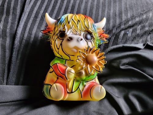 Customer's colorful cow figurine in a stained-glass style, sitting on a dark surface and holding a sunflower.