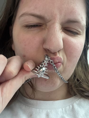 Customer holding a silver mystery pendant with a skull and spiked ring design.