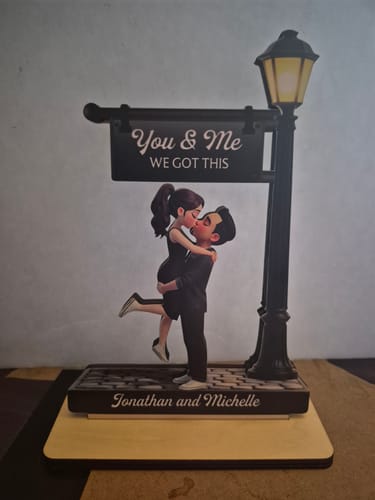 Customer's personalized wooden plaque showing a couple kissing under a lamppost, with 'Jonathan and Michelle' engraved on the base.