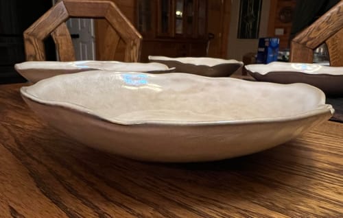 Customer's Crema stoneware deep plates with an organic shape on a wooden dining table.