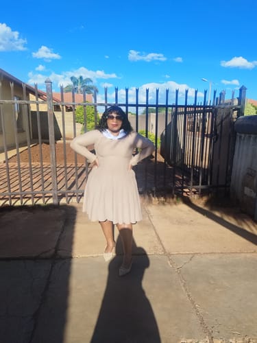 Customer standing outdoors wearing a long-sleeved beige knitted dress with a pleated skirt.