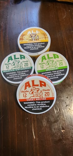 Reviewer's can of Drifters Island Peach pouches displayed with several other ALP flavor cans on a wood table.