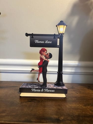Customer's personalized wooden plaque of a couple kissing under a lit lamppost. The base reads 'Maria & Marcus'.