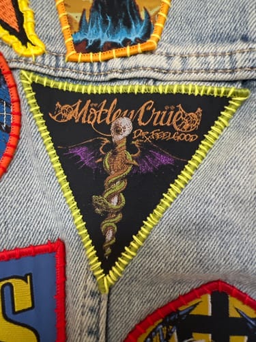 Customer's triangular Motley Crue Dr. Feelgood patch sewn onto a denim jacket with yellow thread.