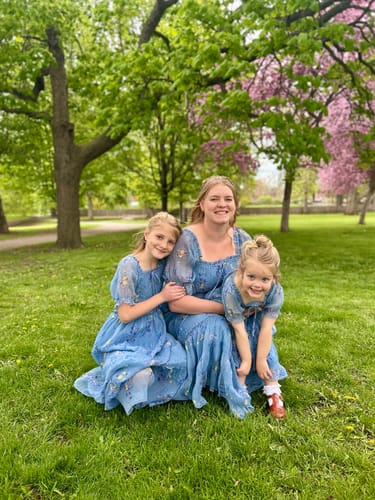 Reviewer and two children in matching dusty blue Crinkled Chiffon Dresses, sitting on a grassy lawn.