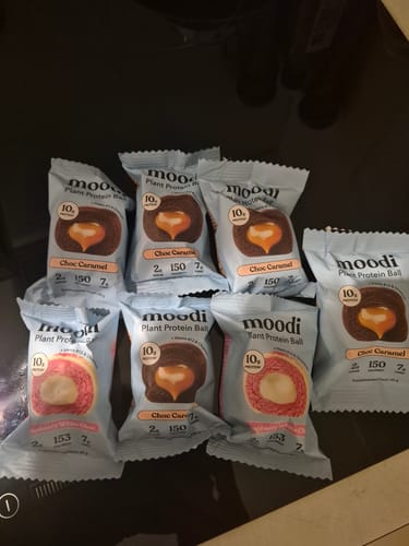 Customer's individually wrapped Plant Protein Balls in Choc Caramel and White Raspberry flavors spread on a surface.